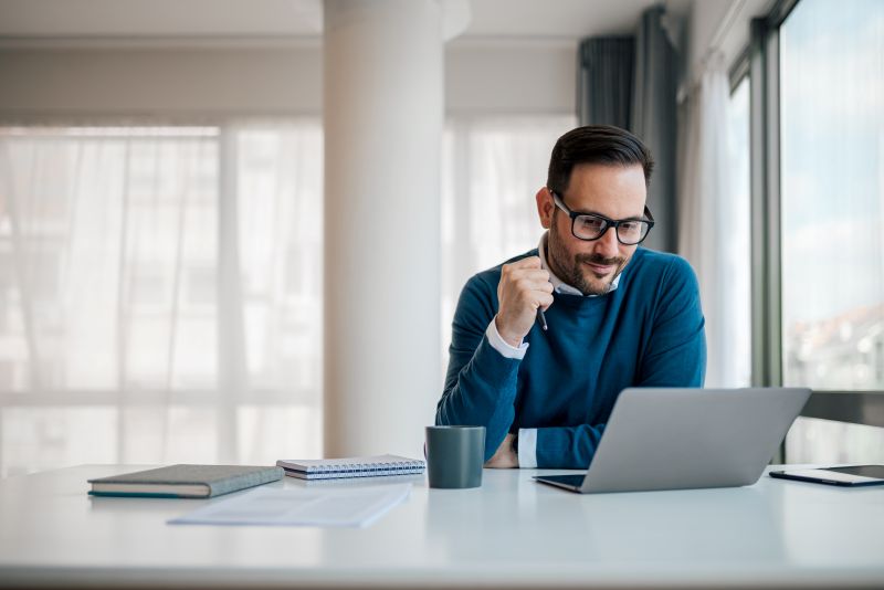 A man in glasses sits at a bright home desk, smiling confidently at his laptop while preparing to file a wage claim online
