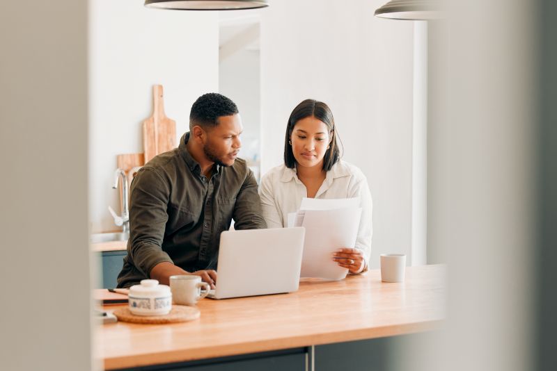 Two people sitting at a kitchen counter reviewing documents together with a laptop open in front of them