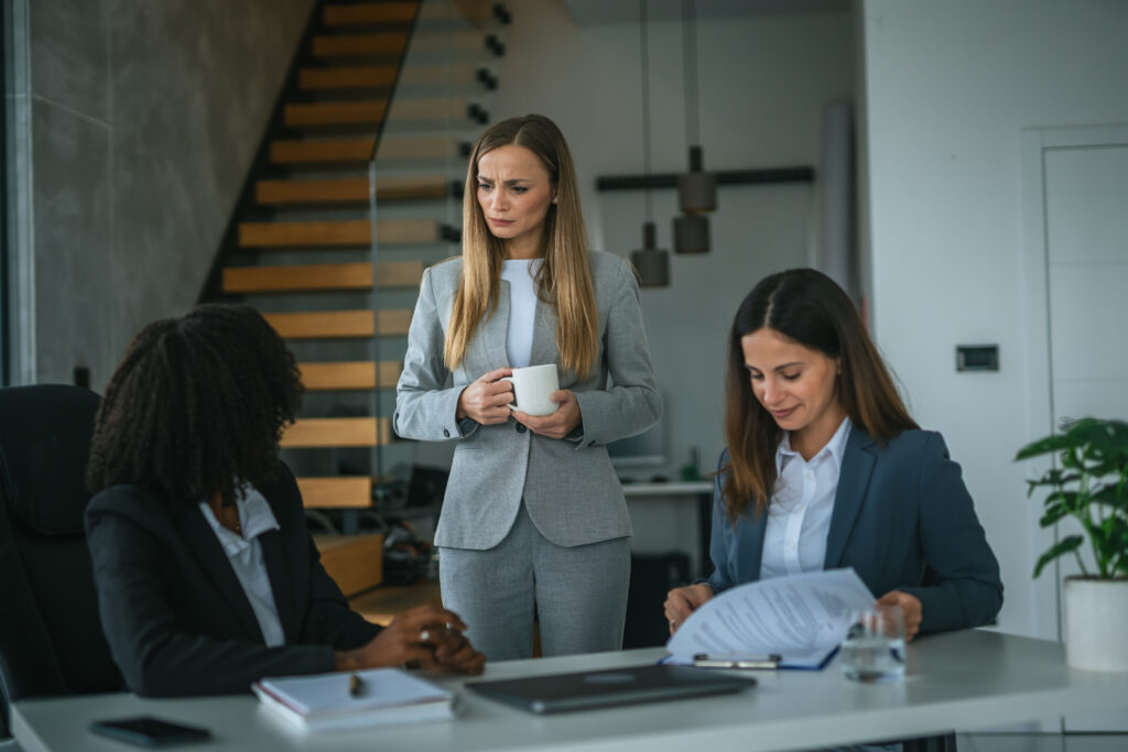 Concerned employee standing in a workplace meeting while colleagues review documents at a conference table