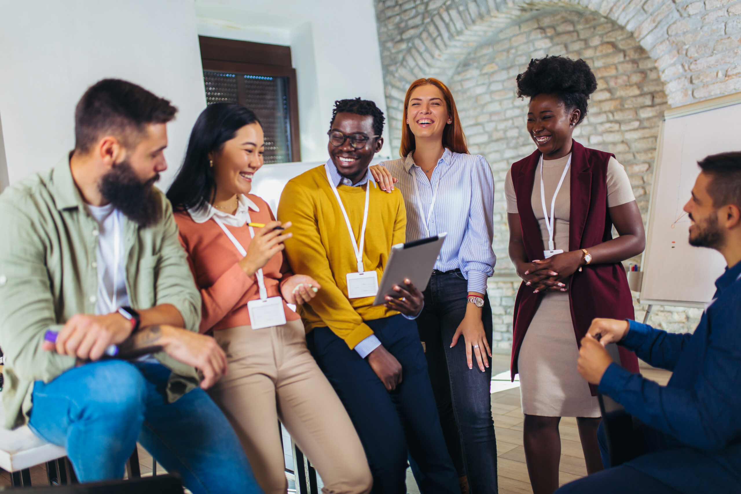A diverse group of six employees wearing work lanyards gathered together in a modern office space, representing coworkers who may share wage and hour claims in a class action.