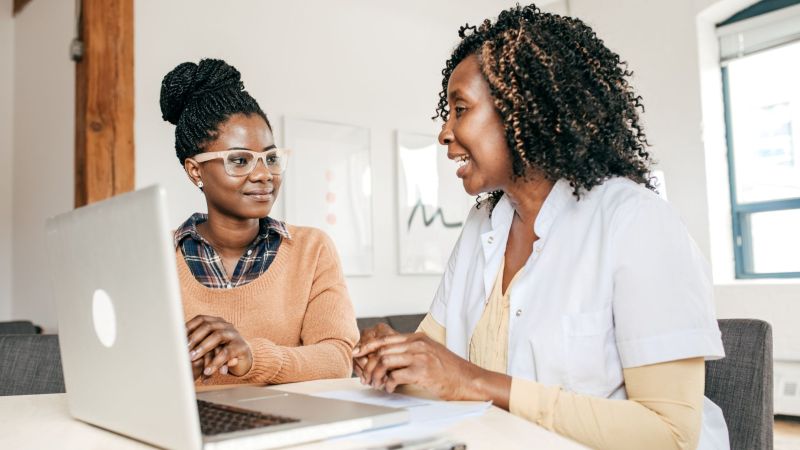 Two women reviewing information together on a laptop, smiling in a bright workspace