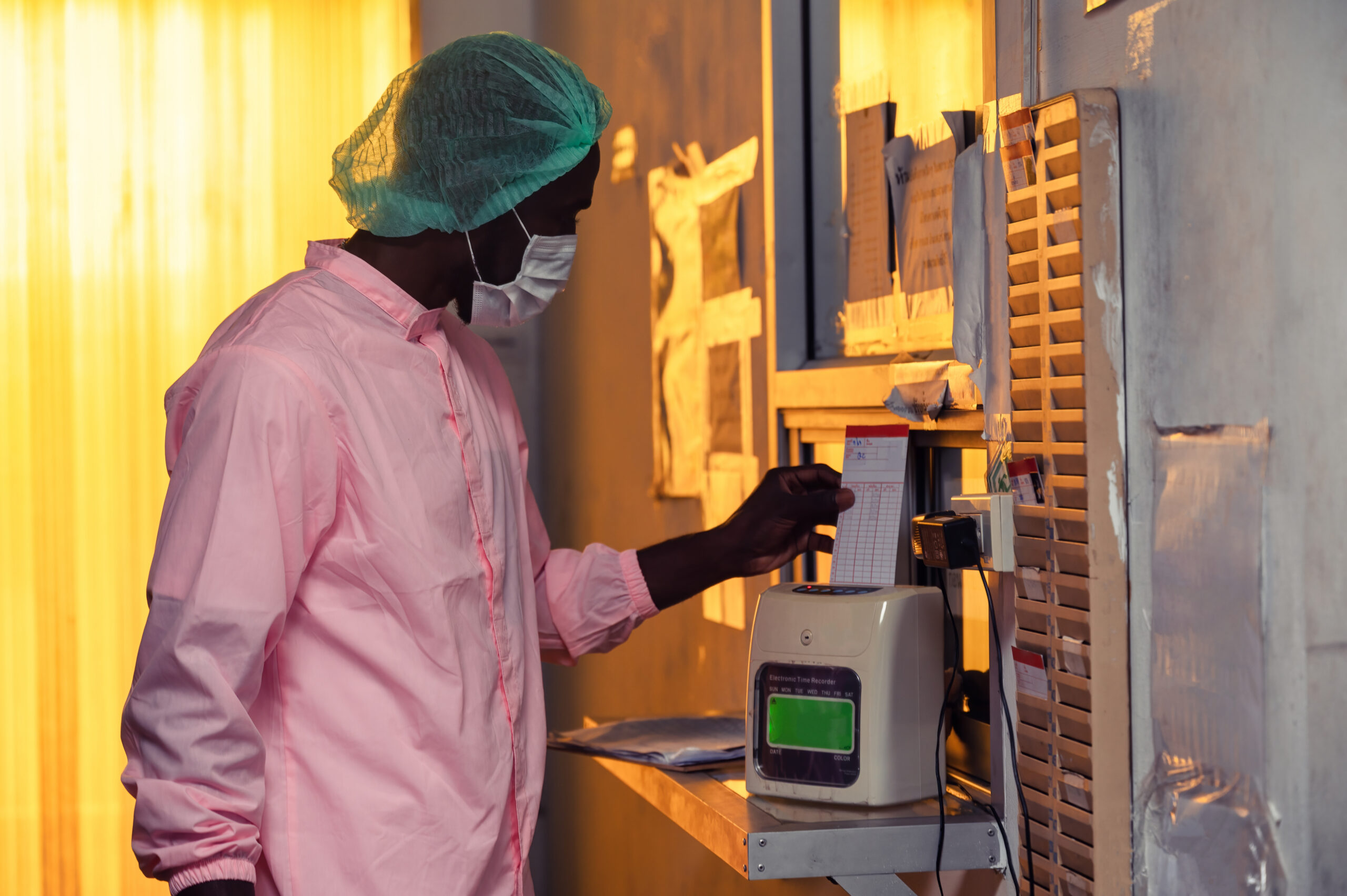 Hourly employee punching a time card at an electronic time recorder before their shift, representing pre-shift off the clock work in California