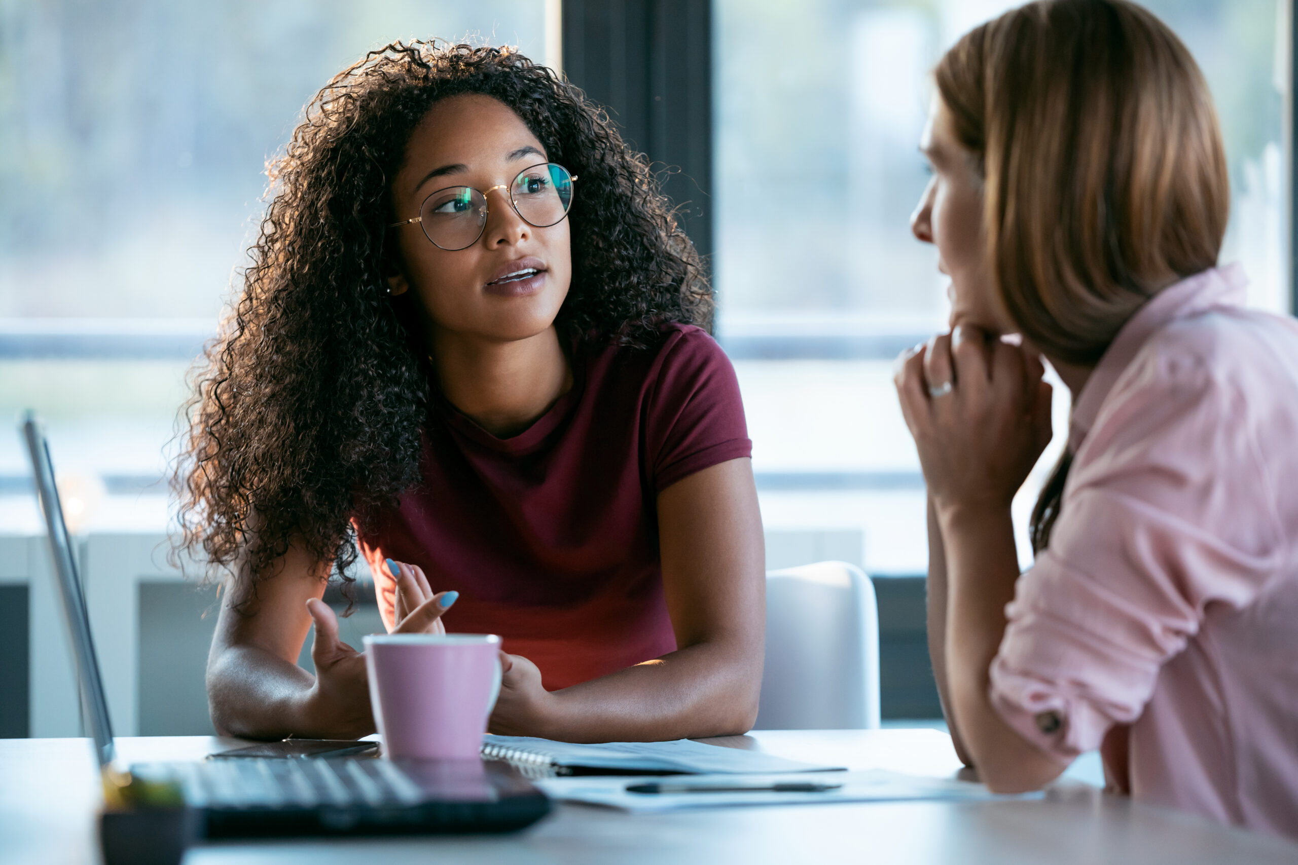 Two women have a focused conversation at a table, one explaining her maternity leave retaliation situation while the other listens carefully
