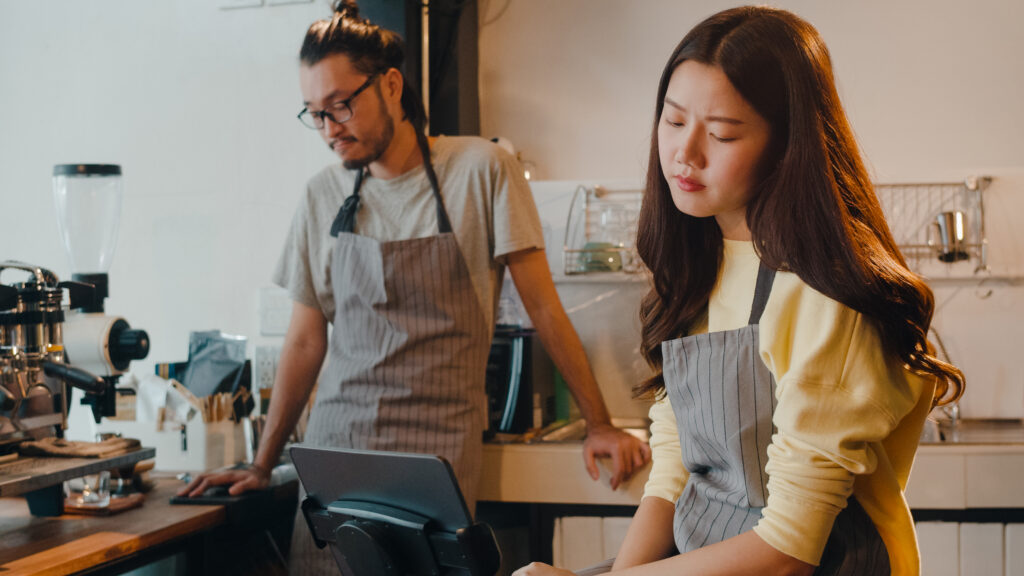 Two café employees in aprons reviewing a point-of-sale system, representing tipped service industry employees navigating tip pooling at work