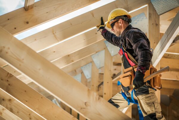 Construction worker in a yellow hard hat and safety harness working on roof framing at a job site, an industry with high rates of independent contractor misclassification in California
