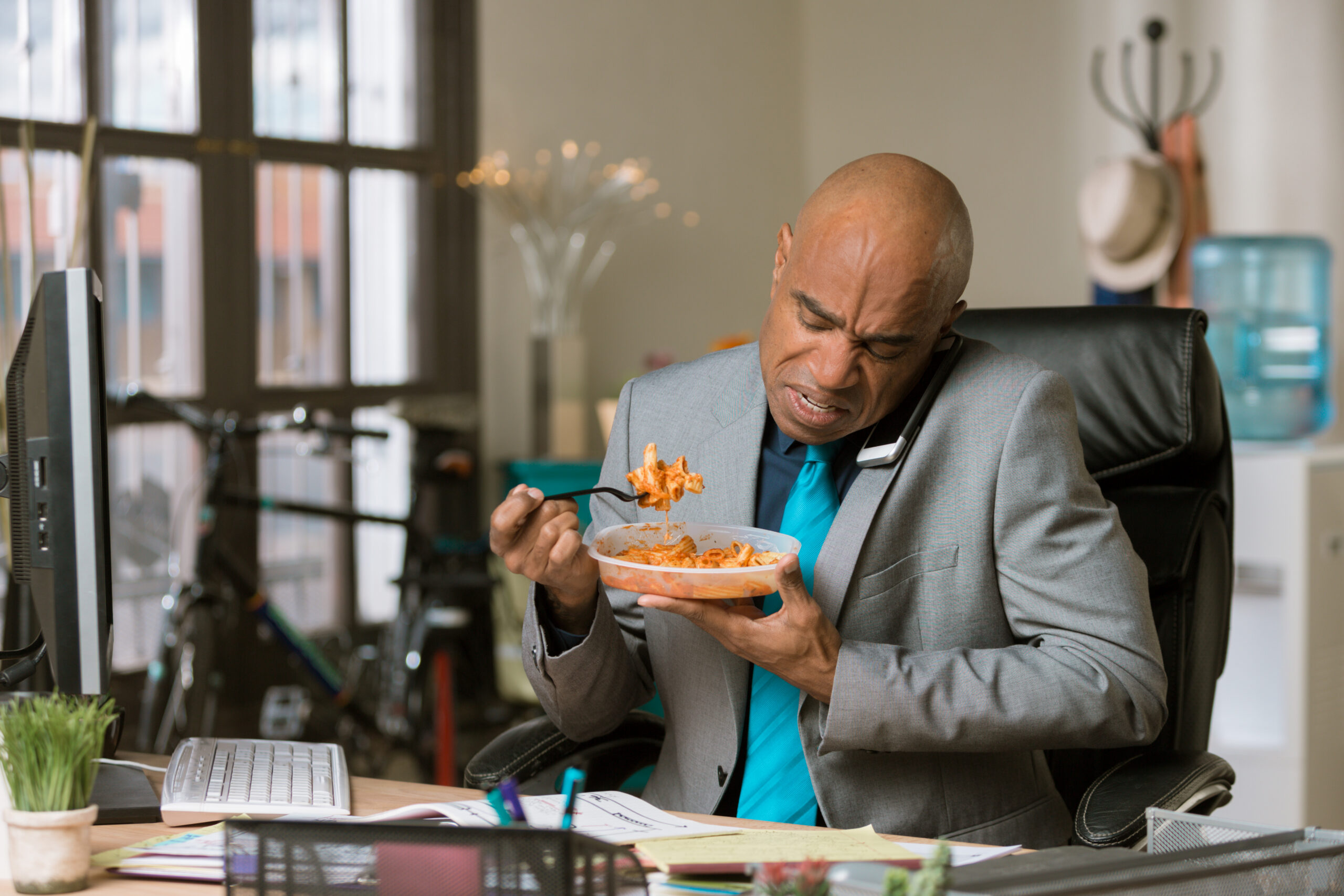 Employee eating lunch at his desk while taking a work call, illustrating an on-duty meal break violation under California break laws