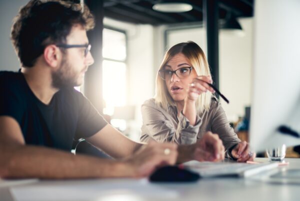 Two employees in a tense conversation at a workplace computer in a wrongful termination and retaliation situation