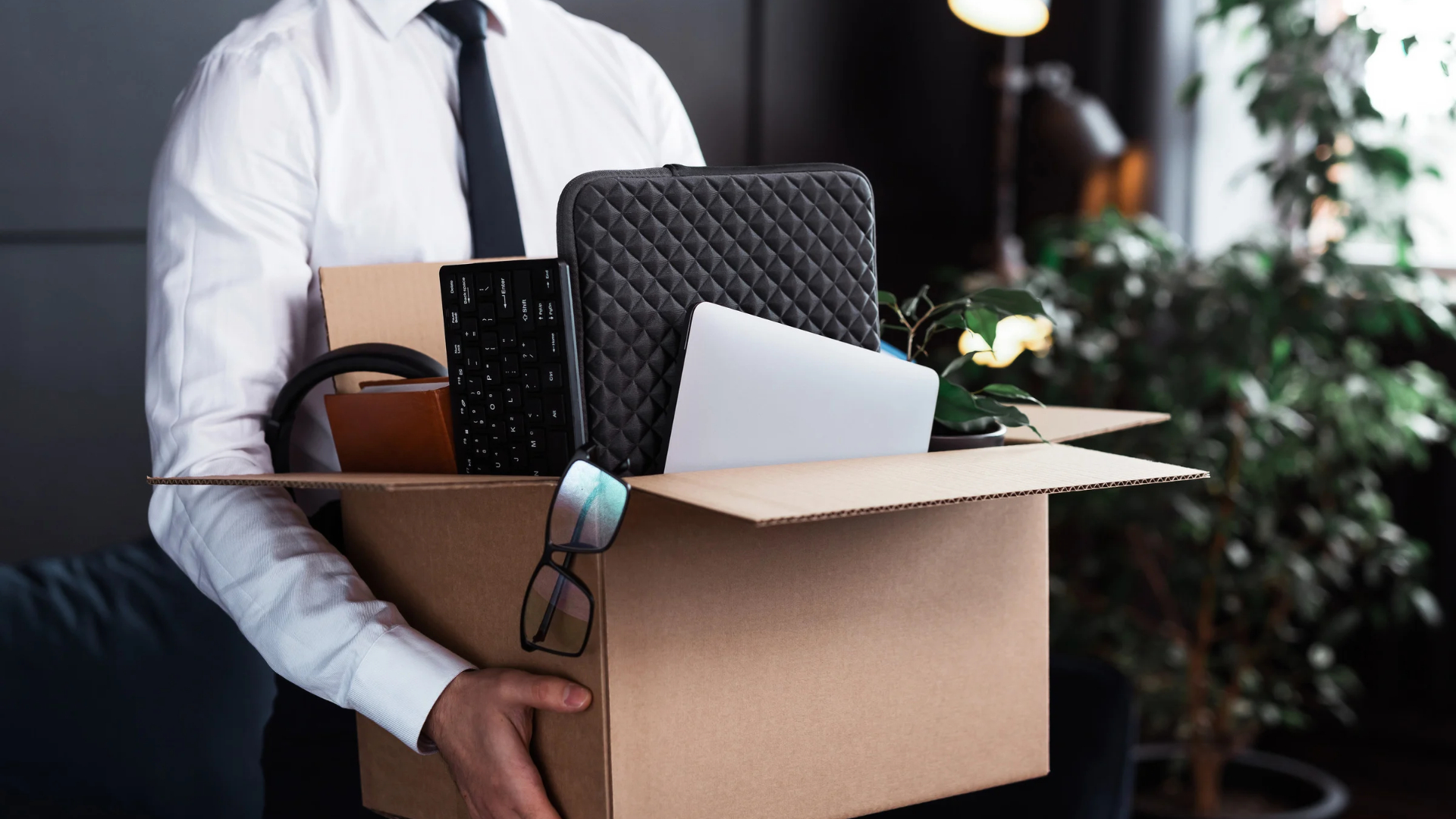 Employee in a white shirt and tie carrying a box of office belongings after a California WARN Act layoff