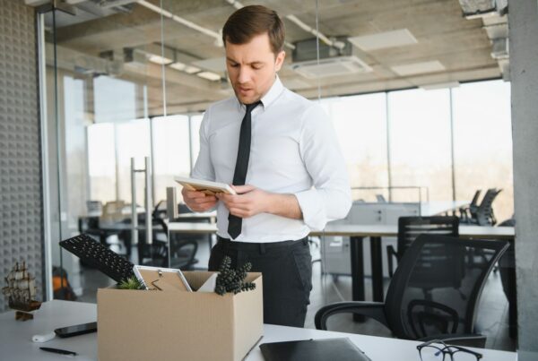 Employee packing personal belongings into a box at his desk in an empty office after being laid off in California