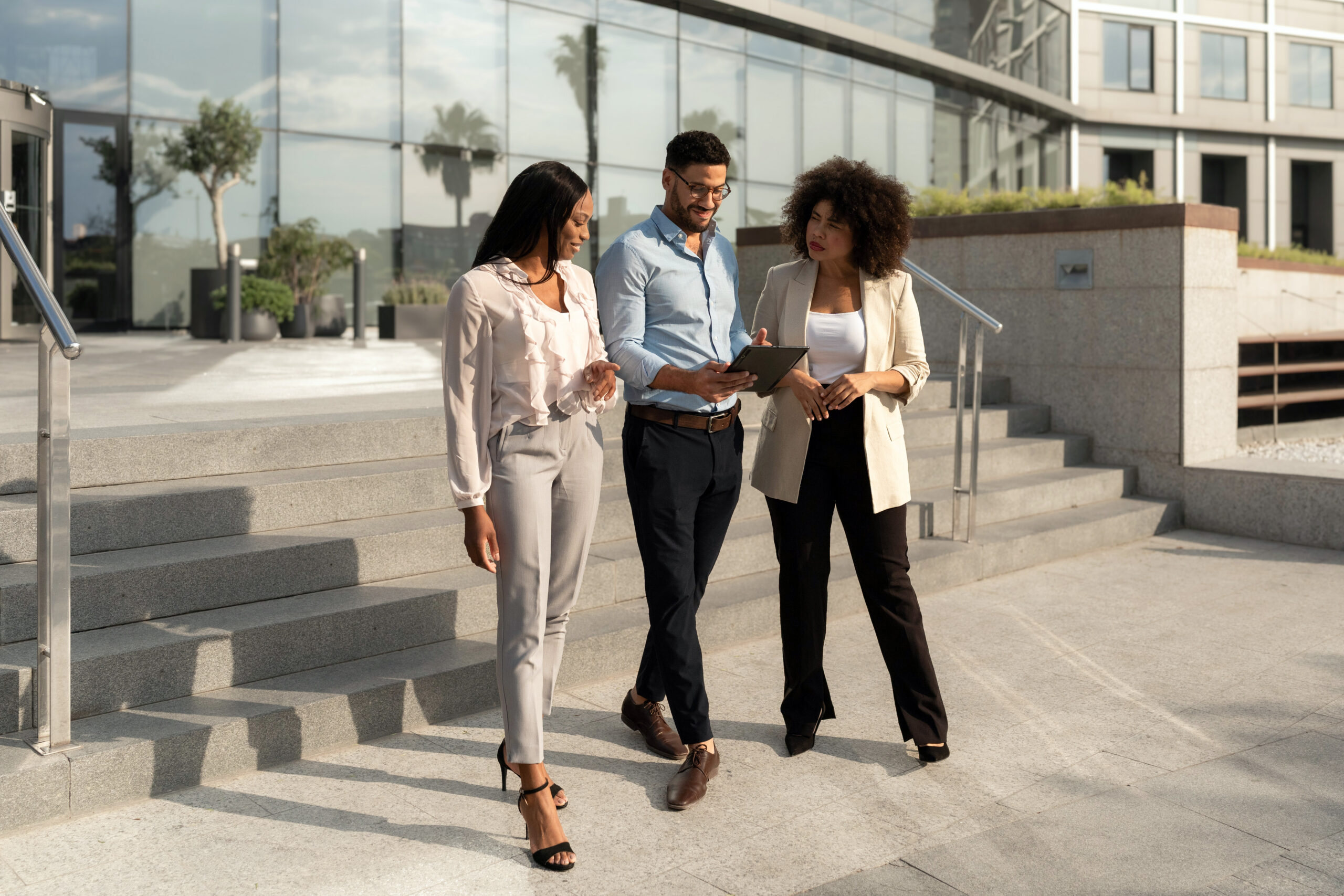 Three employees walking together outside a corporate office building, consulting on documents in discussion