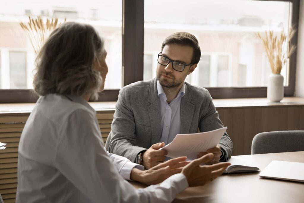 An attorney in glasses reviews documents and listens attentively as an employee explains their situation across a desk during a professional consultation