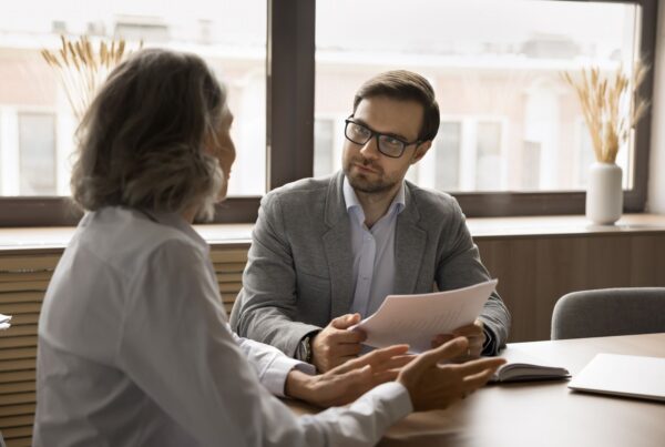 An attorney in glasses reviews documents and listens attentively as an employee explains their situation across a desk during a professional consultation