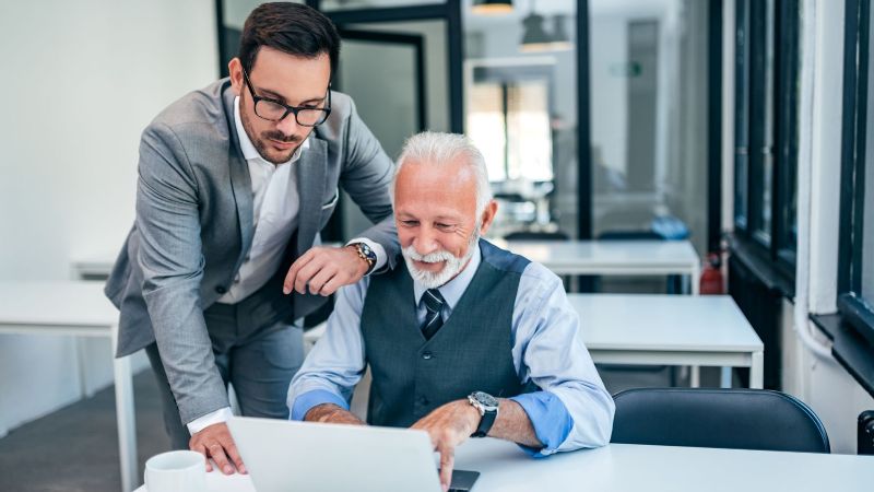 Signs of age discrimination workplace dynamic — older employee and younger colleague at work in California
