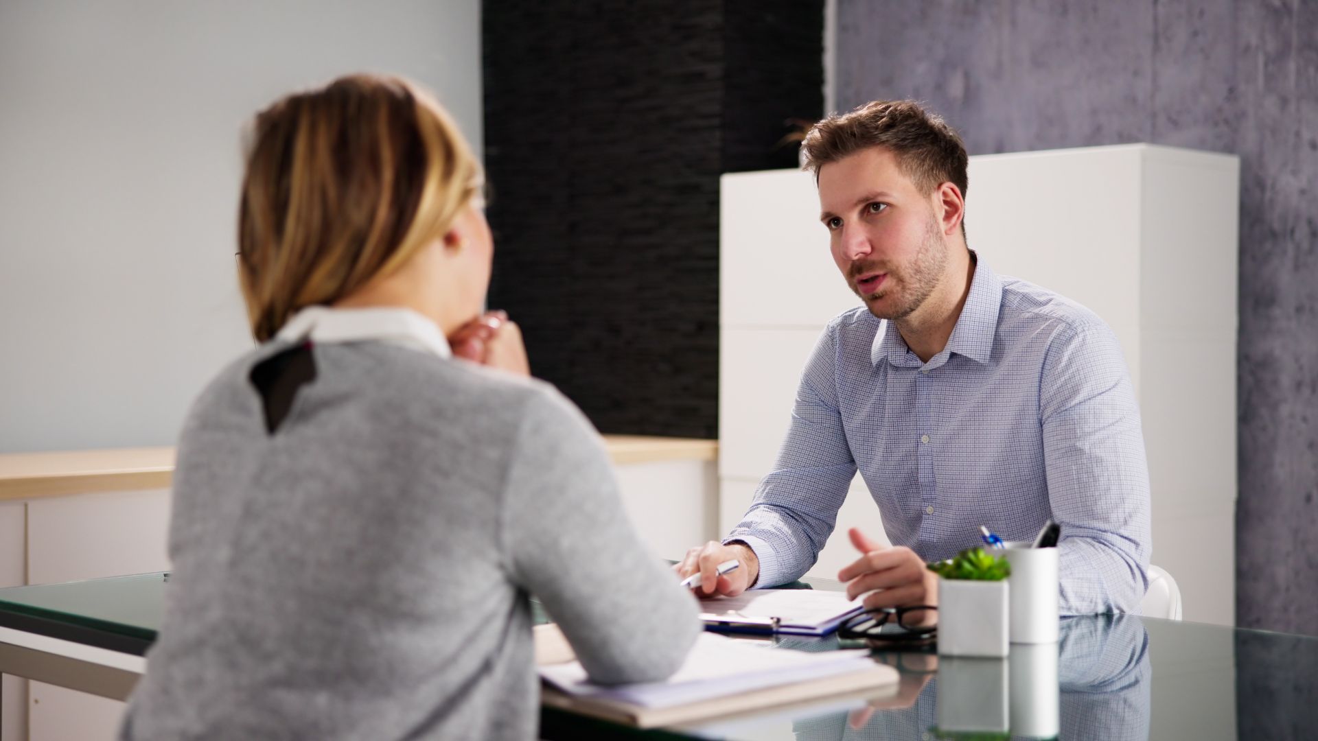 An employee and an employment attorney sit across from each other at a desk in a consultation, with documents and a notepad on the table between them