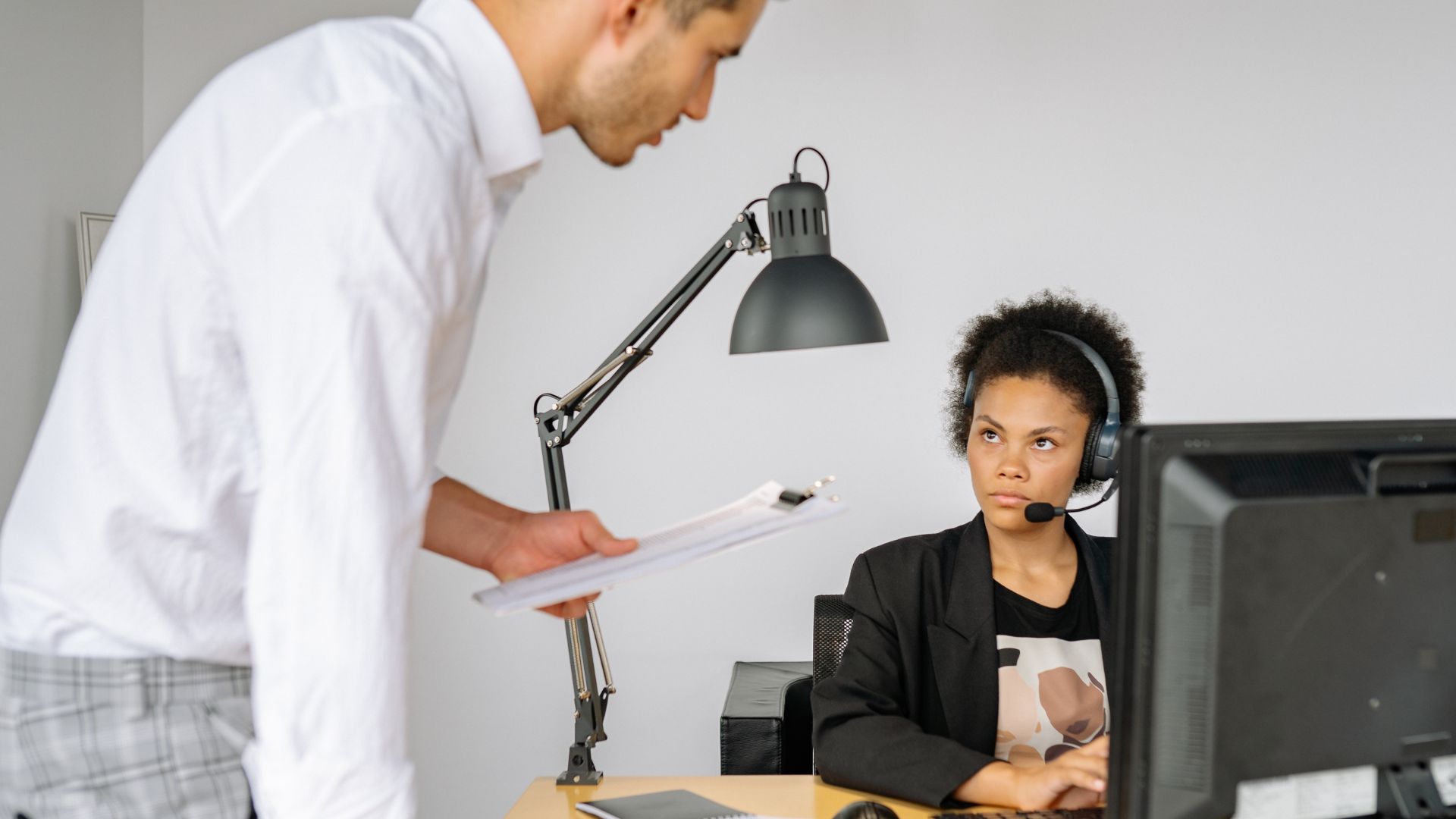 Supervisor standing over employee at desk in tense workplace interaction