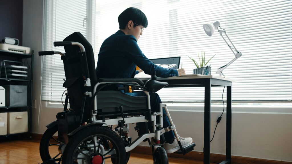 Employee using a wheelchair working at a home office desk while on disability leave in California