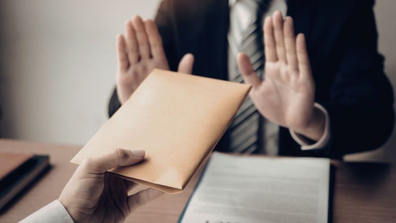 A professional raises both hands to refuse an envelope being handed across a desk, the kind of refusal at the center of a Tameny claim in California