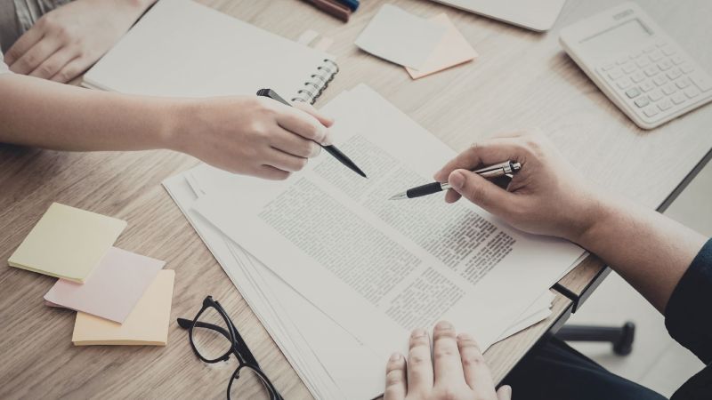 Two people reviewing employment documents with pens, representing the written policies and records that support an implied employment contract claim in California