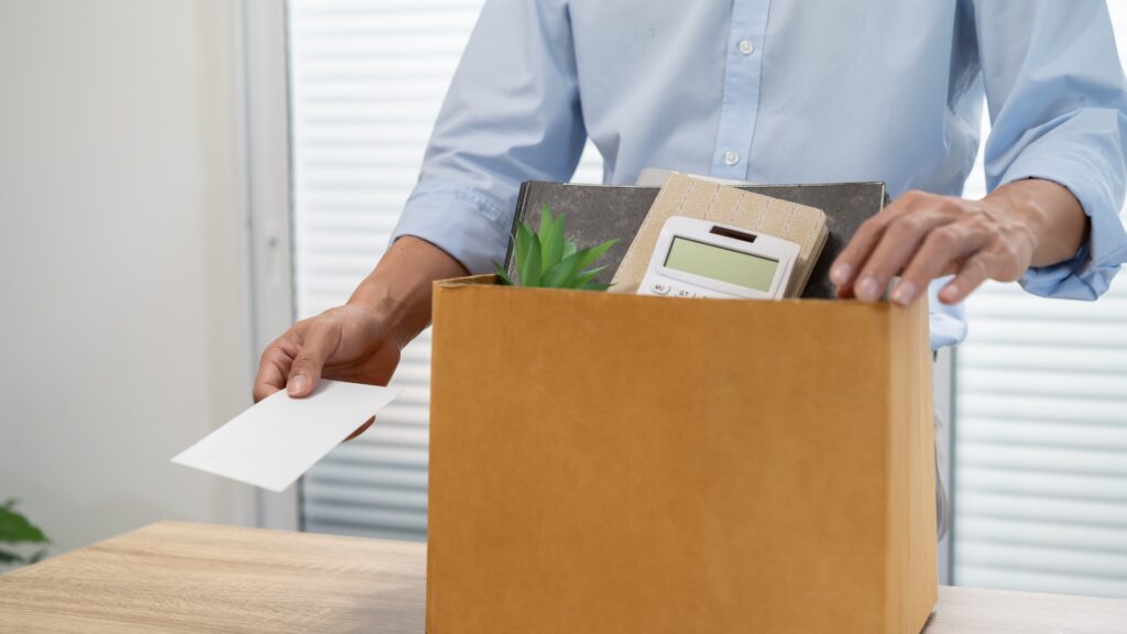 Employee being handed a wrongful termination layoff notice with personal belongings packed in the background