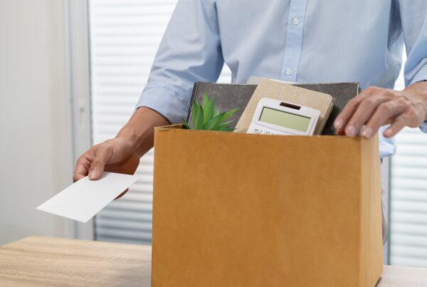 Employee being handed a wrongful termination layoff notice with personal belongings packed in the background