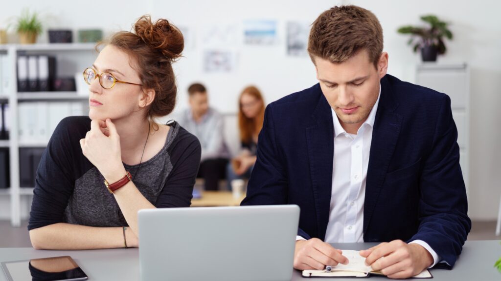 Employee experiencing a hostile work environment — excluded by a coworker at her desk while others meet nearby
