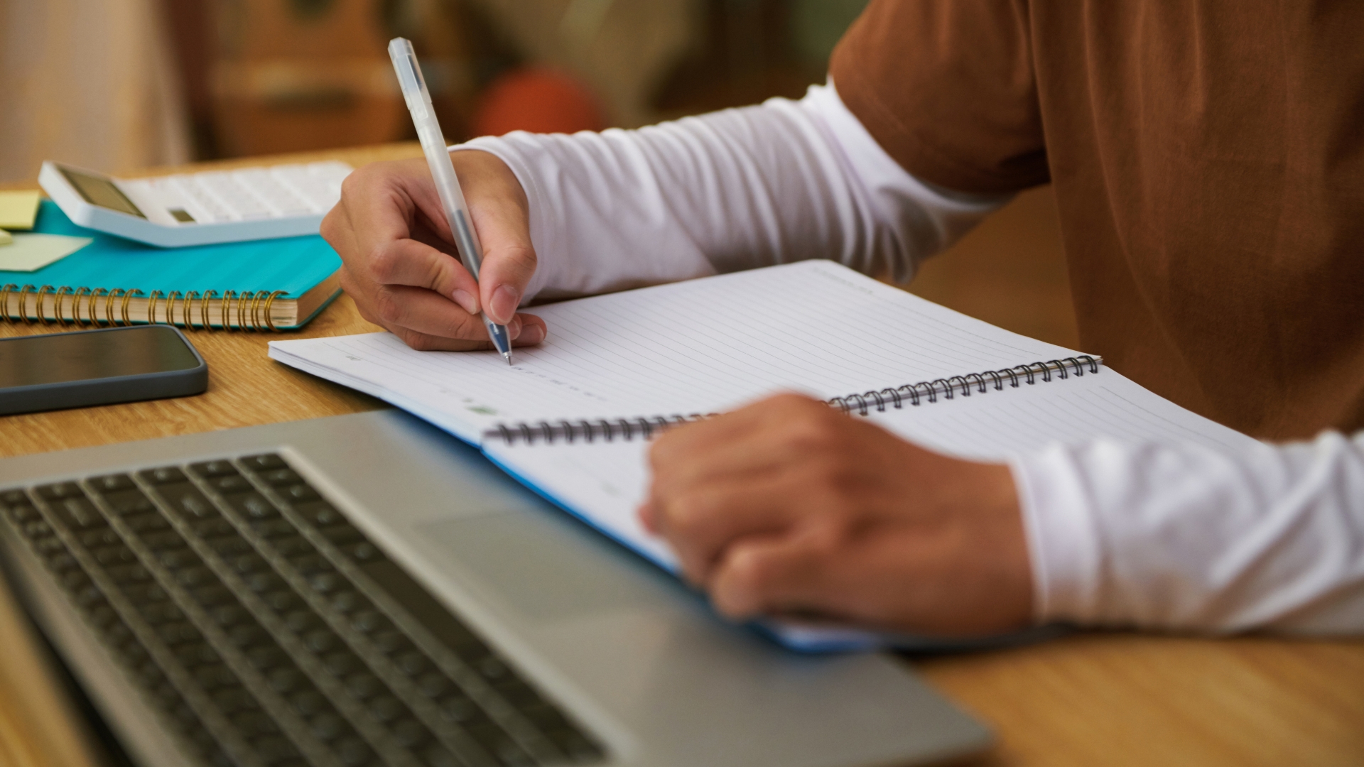 Close-up of hands writing in a spiral notebook beside a laptop, the kind of dated documentation that supports a hostile work environment claim in California