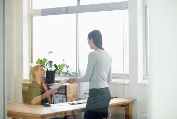 Boss handing a pay rate change notice to a seated employee in a California office