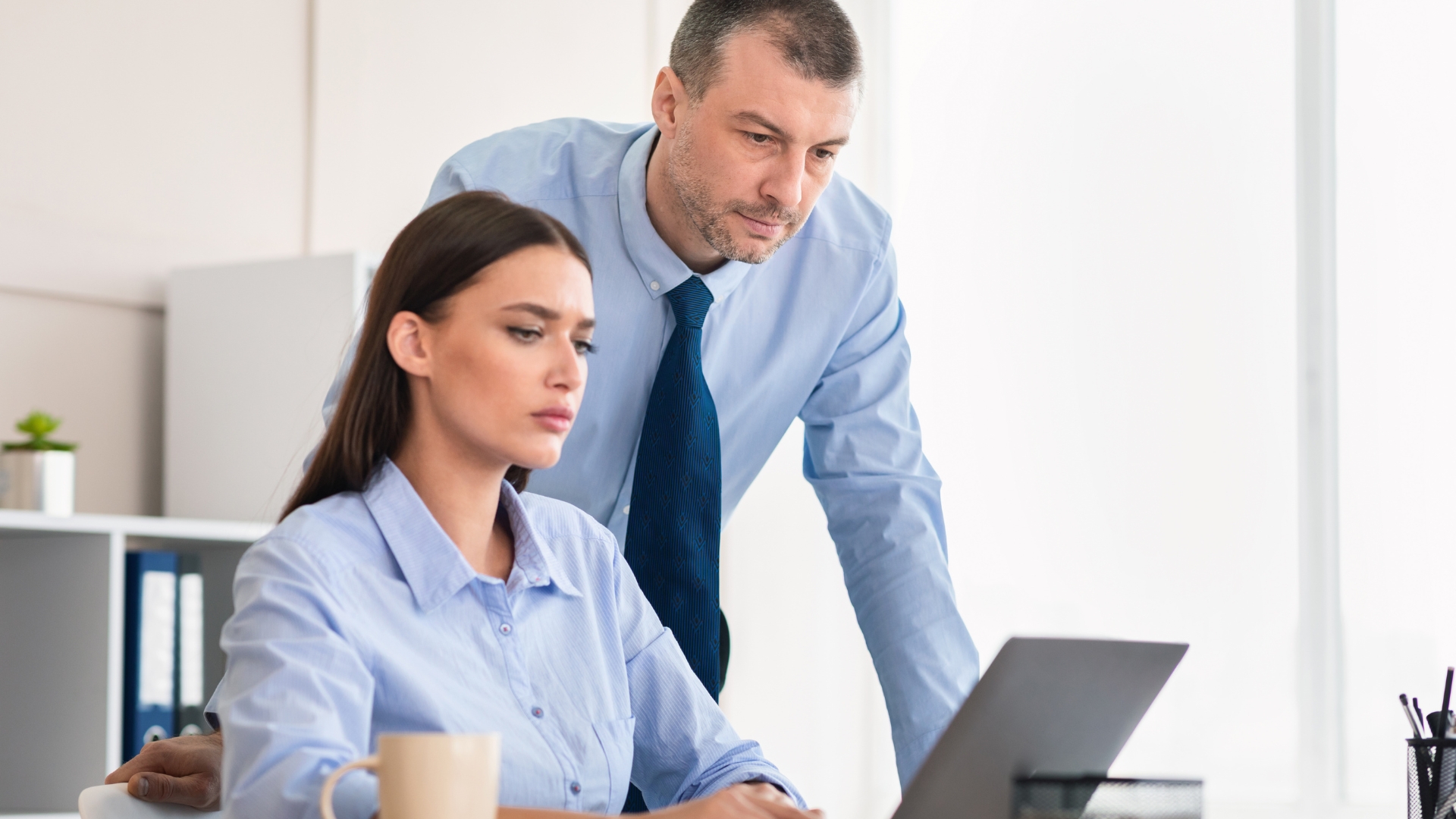 Male supervisor hovering over a female employee at her desk — conduct that may create a hostile work environment under California law