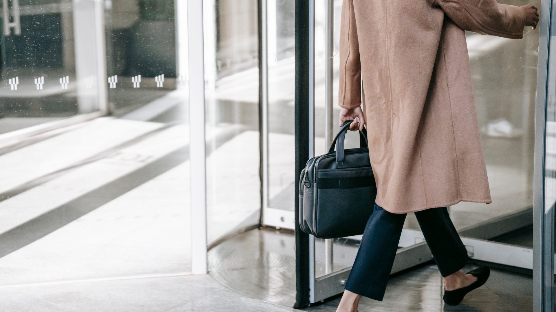 Employee walking into work through a glass office entrance carrying a briefcase — California workers on extended shifts are owed double time pay for every hour past 12