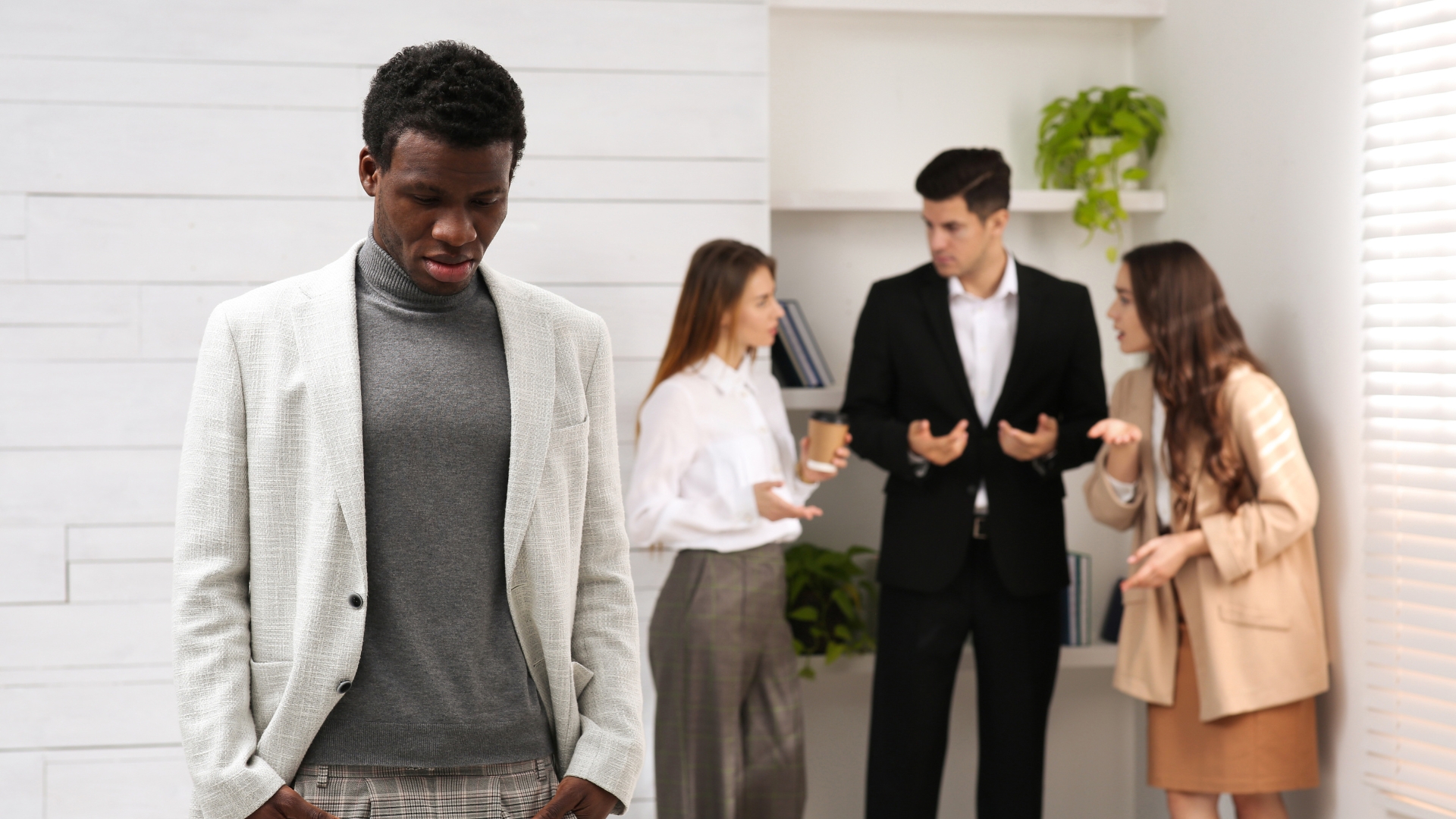 California employee standing apart while coworkers talk behind him, illustrating one of several workplace discrimination examples