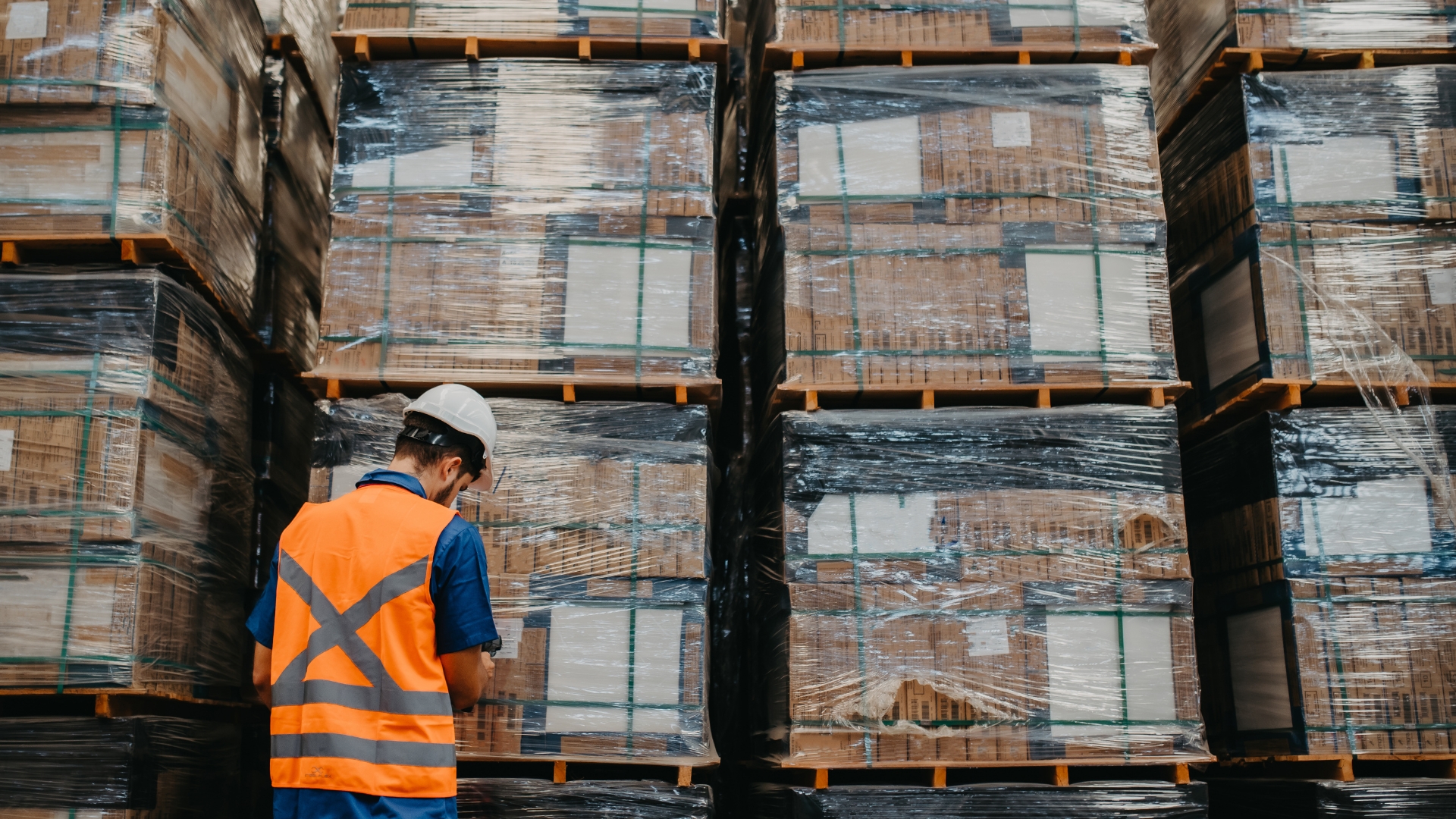 San Bernardino warehouse employee in a hard hat and safety vest checking wrapped pallets