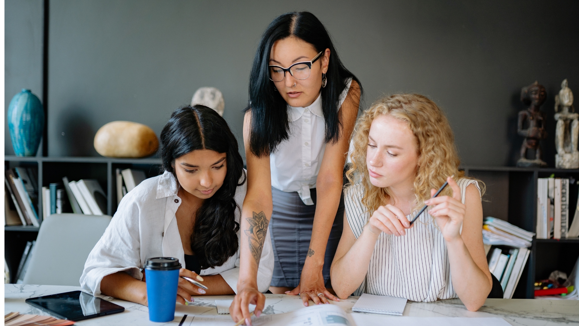 Three coworkers of different backgrounds review paperwork together at a shared office table