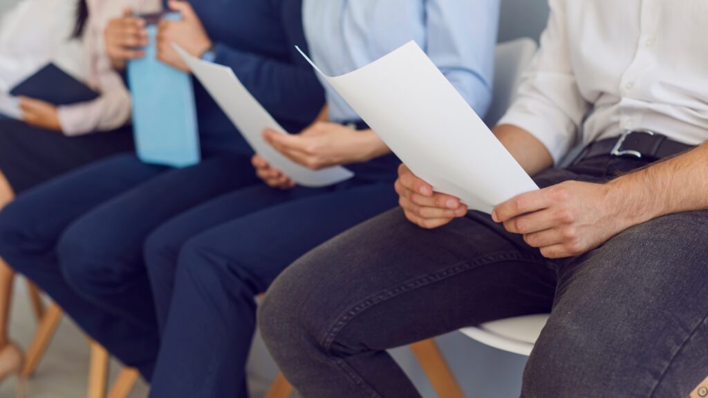 Job applicants holding paper resumes while waiting during an in-person hiring process