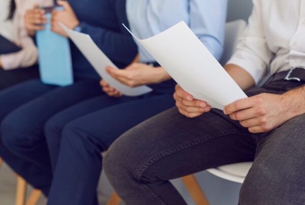 Job applicants holding paper resumes while waiting during an in-person hiring process