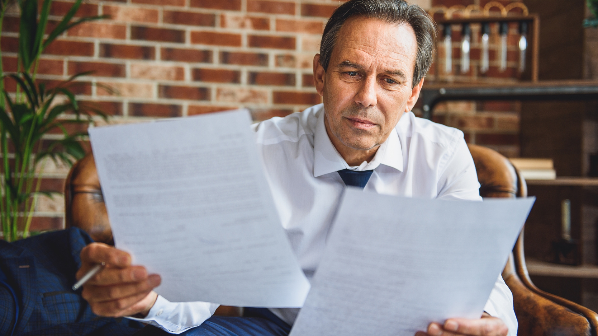 Man reviewing contract paperwork with a concerned expression in an office chair
