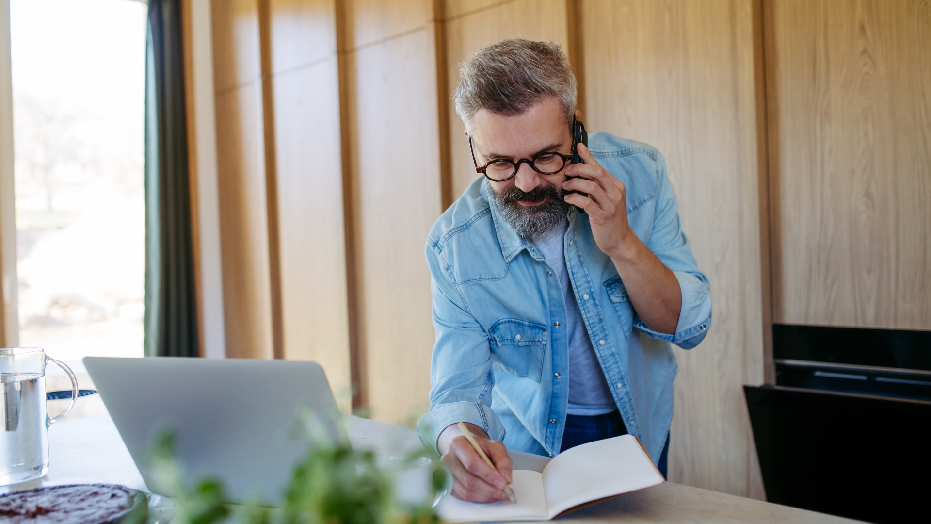 Man taking notes during a phone call at a kitchen table