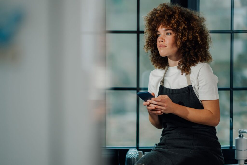 A restaurant worker in an apron pauses during her break to check her phone, wondering about her California overtime pay