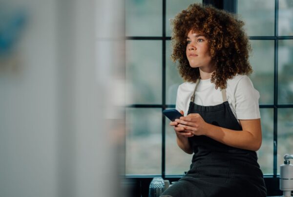A restaurant worker in an apron pauses during her break to check her phone, wondering about her California overtime pay