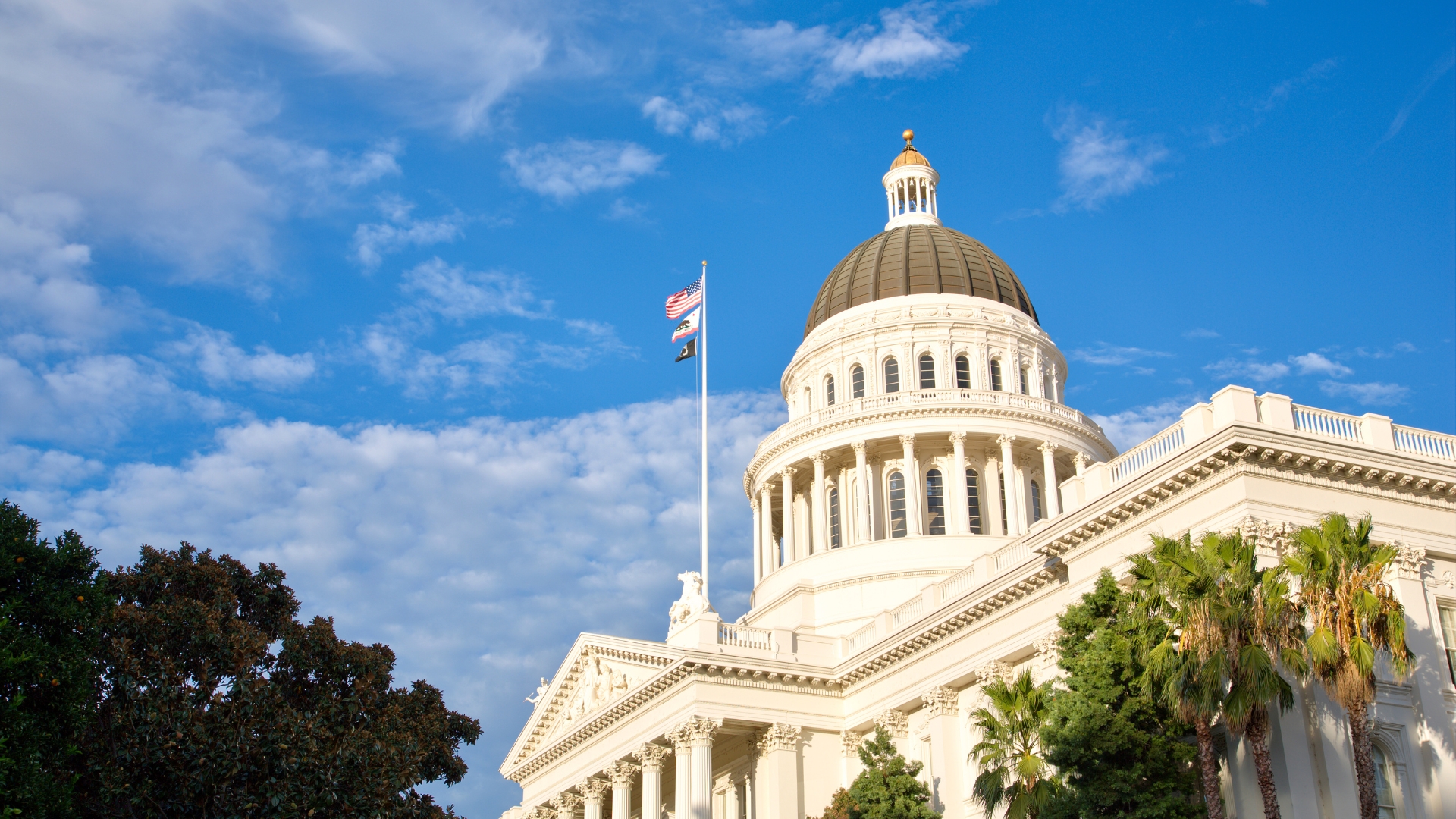 California State Capitol building with the state flag flying under a clear sky