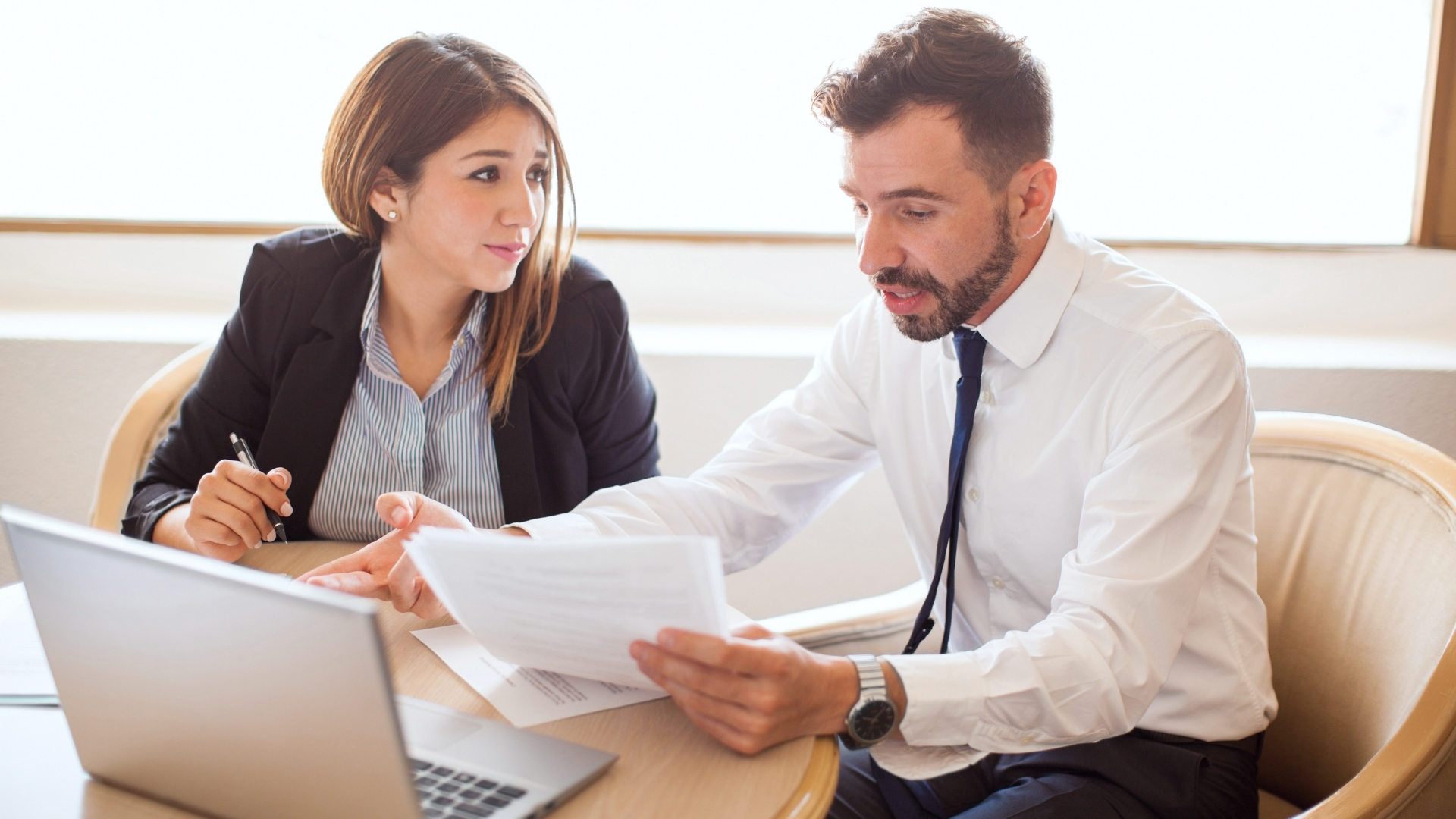 Attorney reviews a document with a client seated at a desk with an open laptop during a consultation.