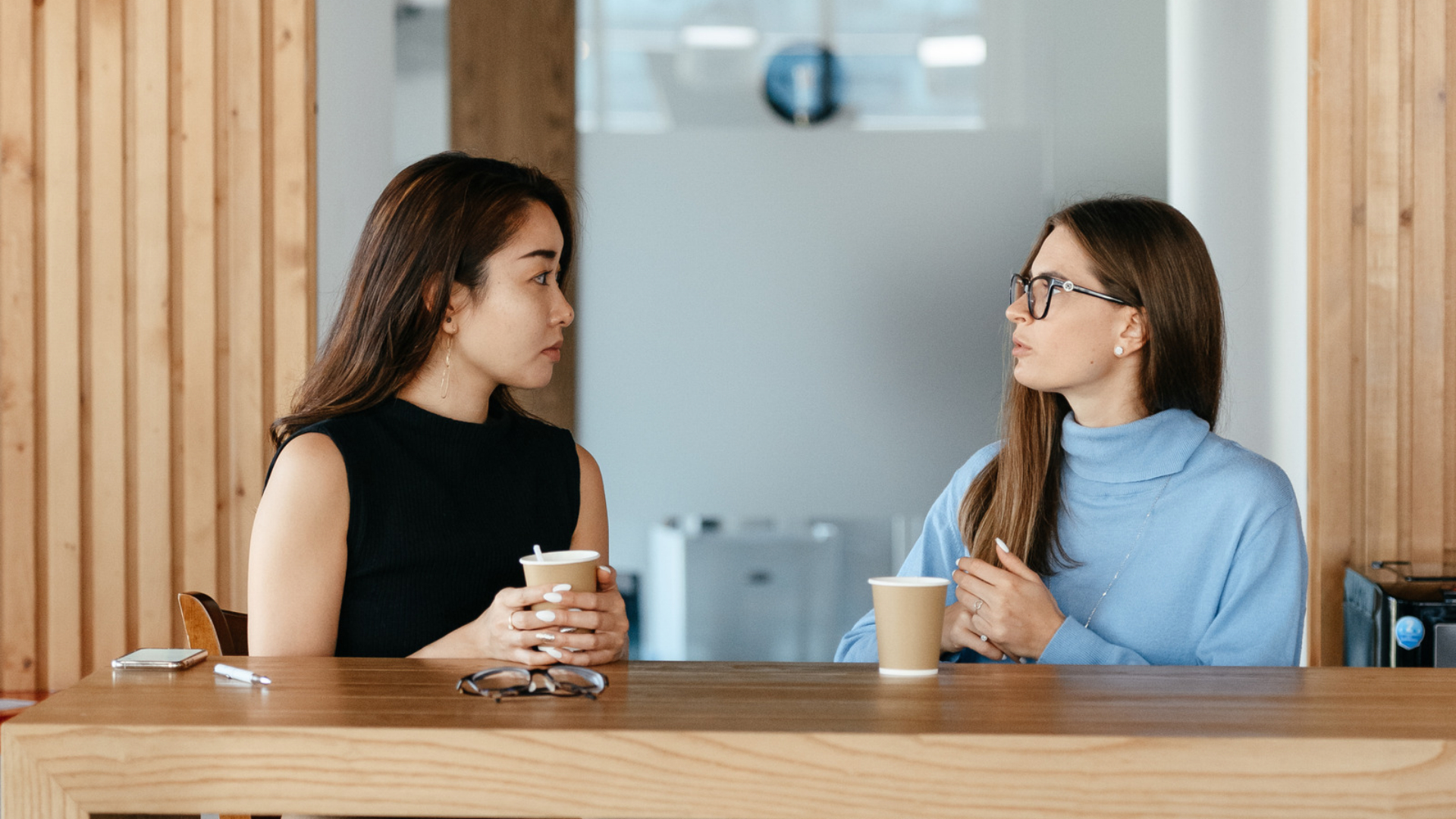 Two coworkers having a serious conversation over coffee in an office break room.