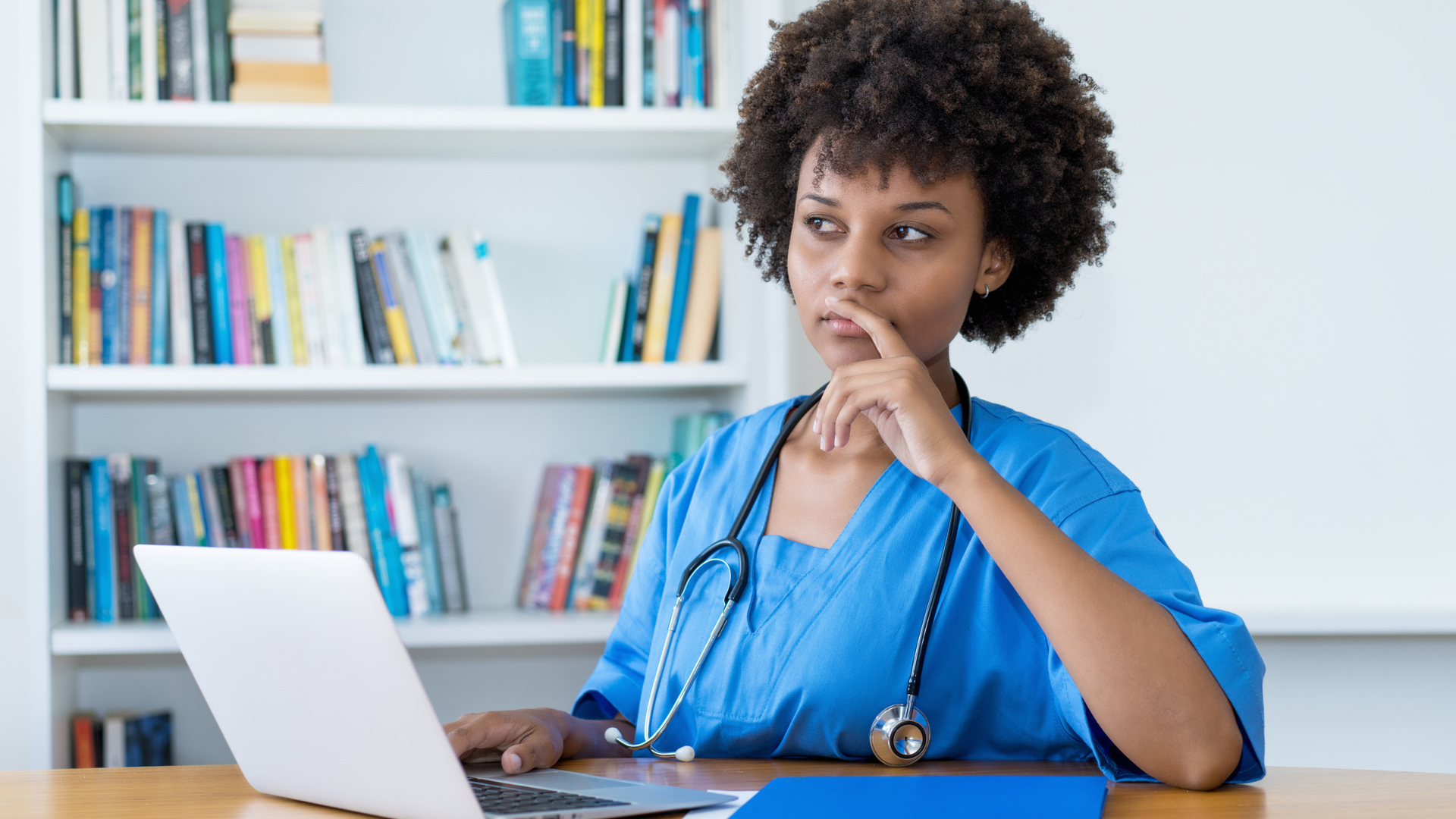 Healthcare employee pausing to think at her laptop while weighing a difficult work decision