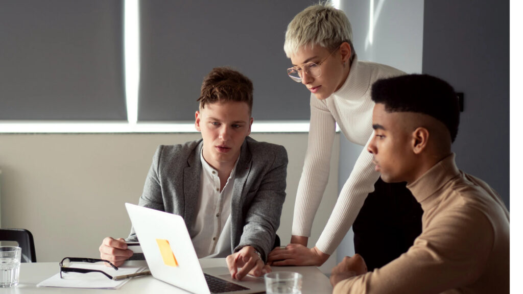 Three coworkers reviewing a laptop together, comparing notes on a workplace issue