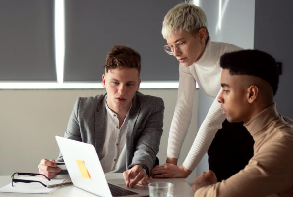 Three coworkers reviewing a laptop together, comparing notes on a workplace issue