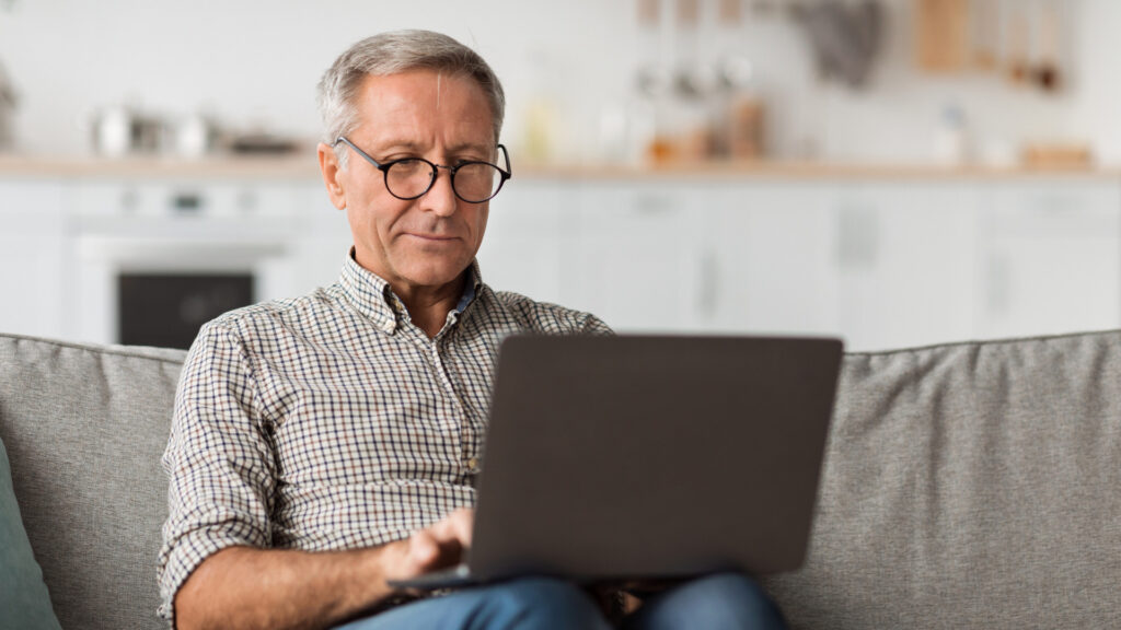 Man in his sixties on a laptop in a sunlit kitchen, researching severance agreement over 40 protections