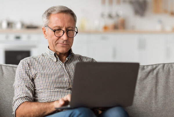 Man in his sixties on a laptop in a sunlit kitchen, researching severance agreement over 40 protections