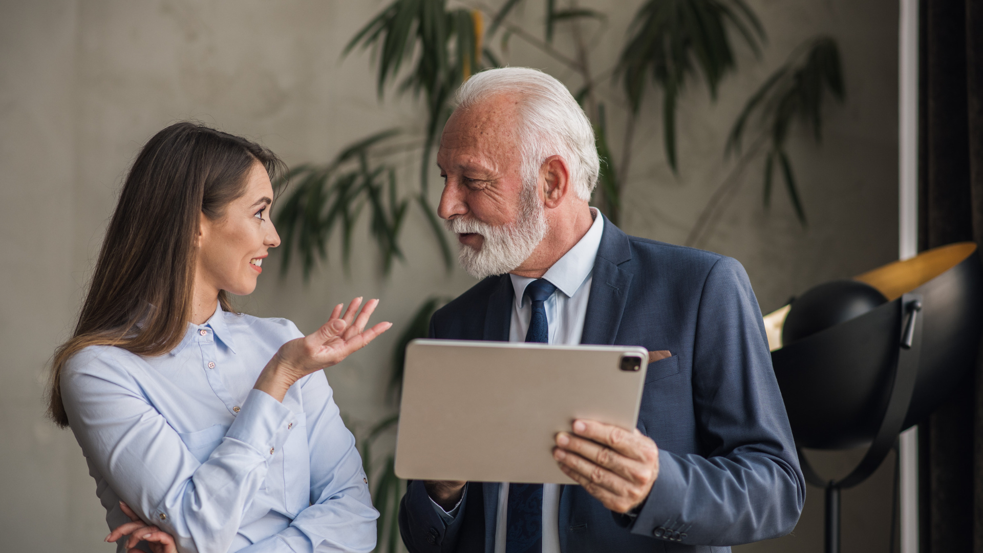 Employee over 40 holding a tablet in conversation with a younger colleague in a modern office
