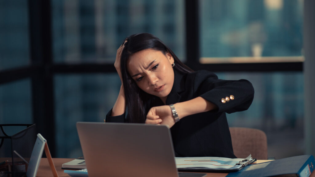 An employee glancing at her watch late at night, still working off the clock at her laptop.
