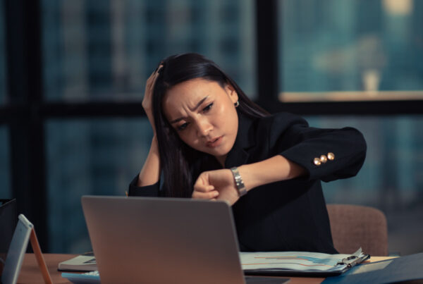 An employee glancing at her watch late at night, still working off the clock at her laptop.