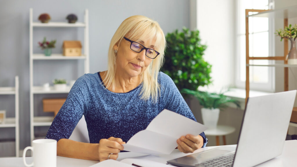 Woman at a home desk reading a printed rejection letter beside her open laptop